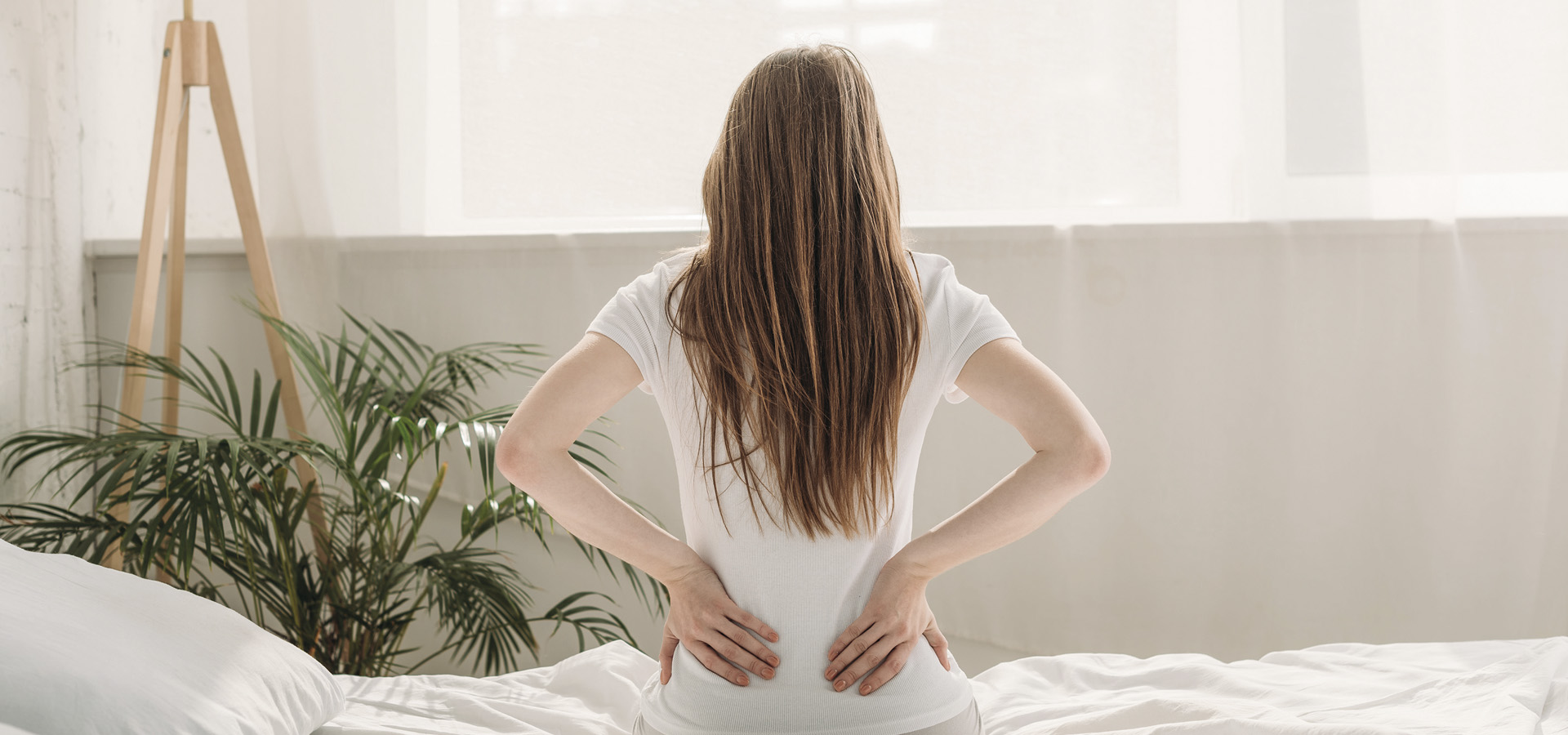 back view of young woman sitting on bed and suffering from back