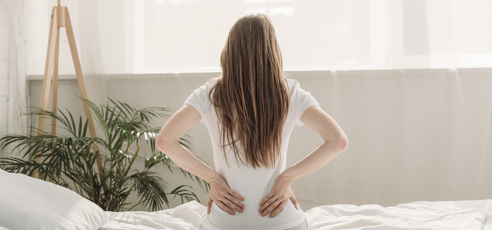 back view of young woman sitting on bed and suffering from back pain